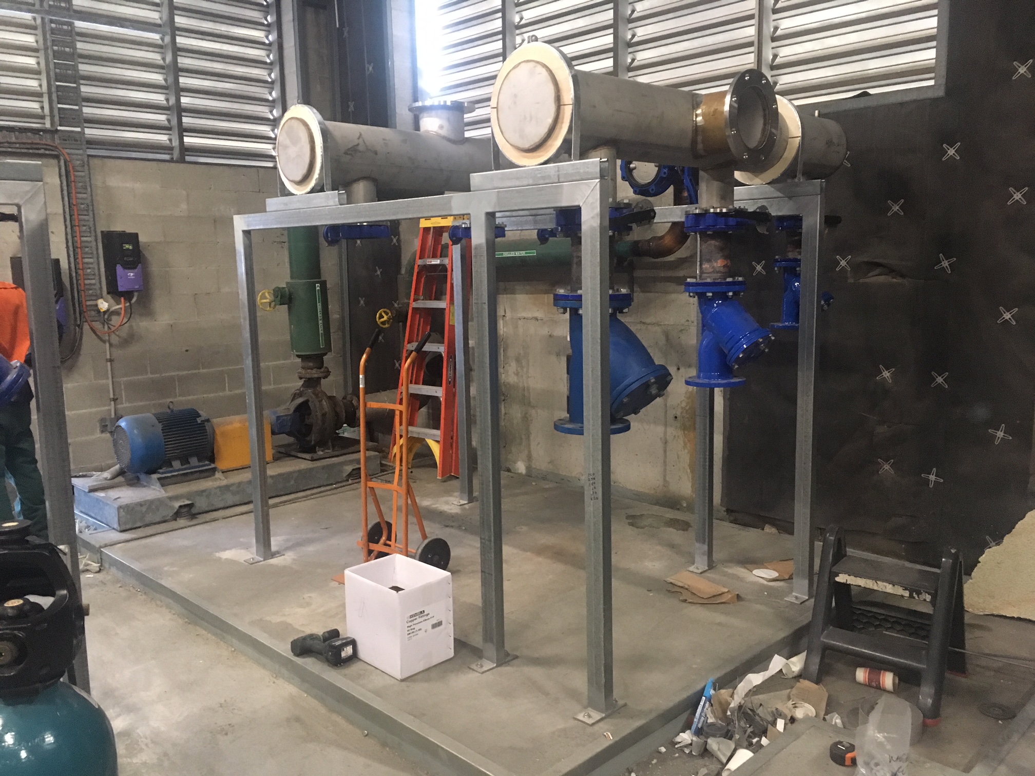 Large-bore chilled water header pipework and galvanised steel support frame under installation in the Northtown plant room, with a DN200 blue butterfly valve and existing pump visible.